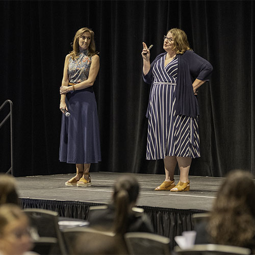 Two people present on stage to a seated audience