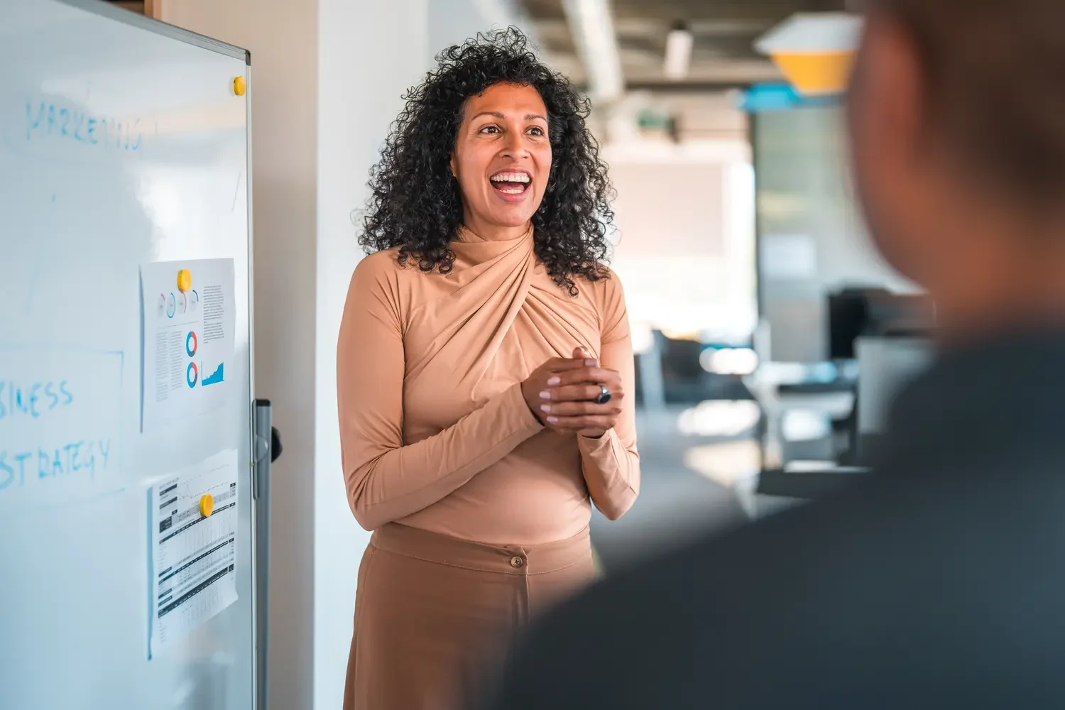 Hispanic office employees brainstorming in a business meeting. They are standing, discussing a strategic plan and looking at a white board.